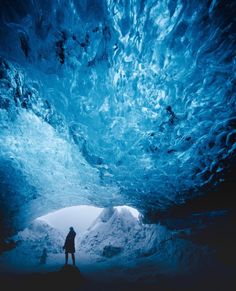 a man standing in the middle of a blue ice cave