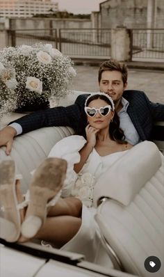 a man and woman sitting on top of a white car with flowers in the back