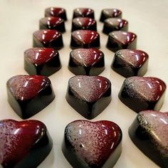 many chocolates are arranged in the shape of hearts on a white counter top with red and black glaze