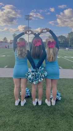 three girls in cheerleader outfits are standing on the field with their hands over their heart