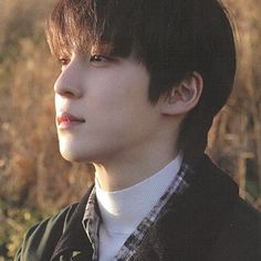 a young man standing in a field with tall grass and weeds behind him, wearing a black jacket