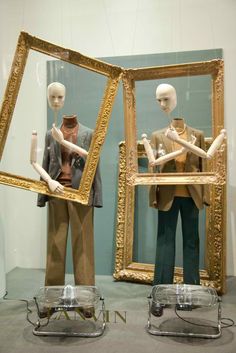 two mannequins are standing in front of three frames with clothes on them