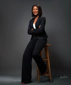 a woman sitting on top of a wooden chair in front of a gray background with her arms crossed