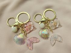 two mermaid themed key chains with seashells attached to them on a white sheet