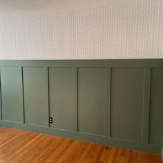 an empty room with green paneling and wood floors