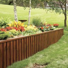 a long wooden planter filled with lots of flowers next to a lush green field