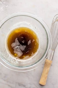 a glass bowl filled with liquid next to a whisk on top of a counter