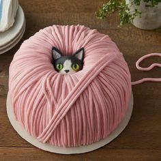 a pink yarn ball cake with a cat's head sticking out of it