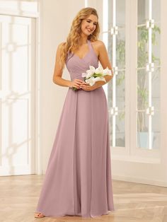 a woman standing in a room wearing a long purple bridesmaid dress and holding flowers