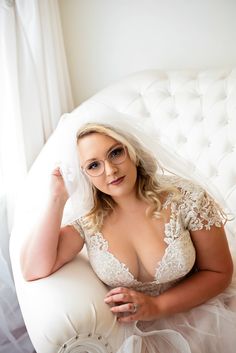 a woman sitting on top of a white couch in a wedding dress and holding her veil over her head