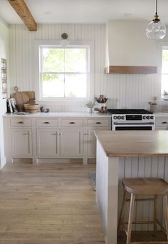 a kitchen with white cabinets and wood flooring next to an island in front of a window