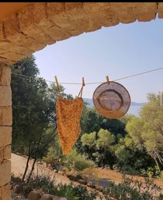 two towels hanging on a clothesline outside by some rocks and trees with the ocean in the background