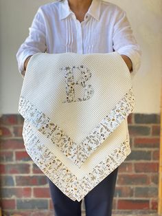 a man holding up a white crocheted blanket with the letter d on it