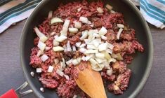 meat and onions cooking in a pan with a wooden spoon