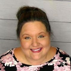 a woman smiling for the camera in front of a white wall with flowers on it