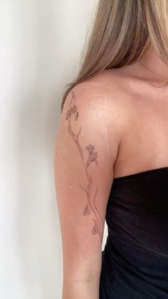 the back of a woman's shoulder with a flower tattoo on her left arm