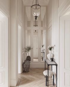 an elegant hallway with white walls and wood flooring, vases on either side of the hall