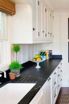 a kitchen with white cabinets and black counter tops is pictured in this image, there are fruit on the counter