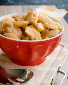 a red bowl filled with bananas on top of a wooden cutting board next to silverware