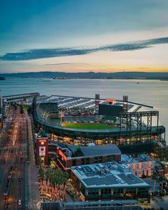 an aerial view of a baseball stadium at dusk with the ocean in the background and lights on