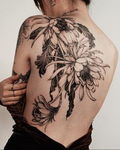 the back of a woman's body with tattoos on it and flowers in bloom