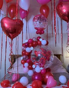 valentine's day decorations with balloons and streamers hanging from the ceiling in front of a bed