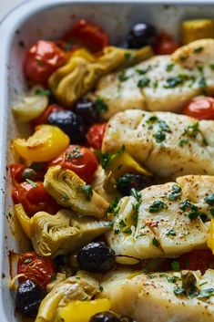 chicken and vegetables in a casserole dish with olives, tomatoes, peppers, and broccoli