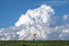 a person holding an umbrella while standing on top of a lush green field under a large cloud