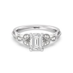 a white gold engagement ring with an emerald center stone surrounded by diamonds on the side