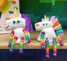 two plastic unicorns sitting on top of a wooden shelf next to each other in front of a colorful wall