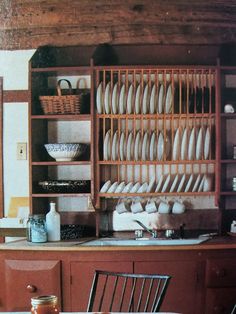 an old fashioned kitchen with plates and dishes on the shelves above the sink, in front of a wooden hutch