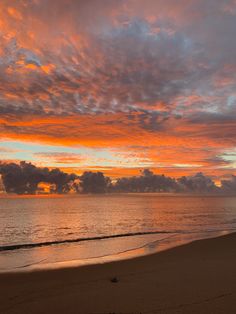 an orange and pink sunset over the ocean with clouds in the sky above it, as seen from a beach at low tide