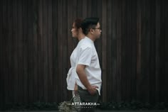 two people walking down the street in front of a wooden fence