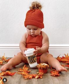 a baby sitting on the floor with a cup of coffee in front of it and leaves all around