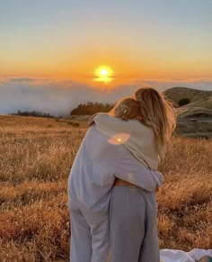 a woman standing on top of a dry grass covered field next to a sun setting