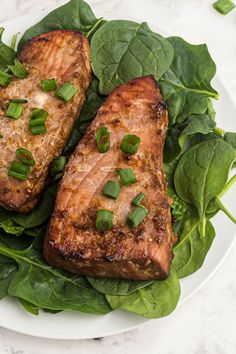 two pieces of meat sitting on top of green leafy greens in a white plate