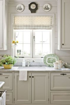 a kitchen with white cabinets and green dishes on the counter top, in front of a window