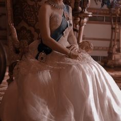 a woman in a dress sitting on a chair wearing a tiara and pearls necklace