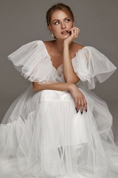 a woman in a white dress posing for the camera with her hand on her chin