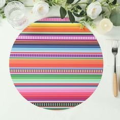 a colorful place mat with stripes and flowers on the table next to utensils