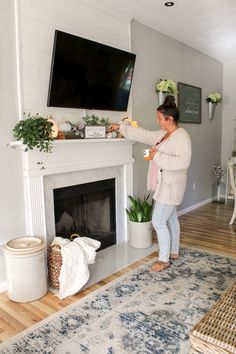 a woman standing in front of a fireplace with a television on it's wall