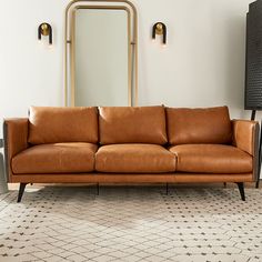 a brown leather couch sitting in front of a mirror on top of a floor next to a lamp