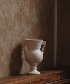 a white vase sitting on top of a wooden shelf