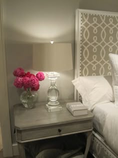 a nightstand with flowers on it next to a bed