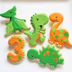 decorated cookies in the shape of dinosaurs on a white plate with green and orange icing