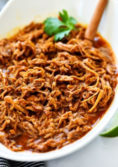 a white bowl filled with shredded meat and garnished with cilantro leaves