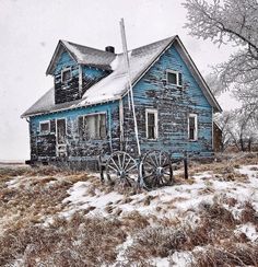 an old blue house sitting in the middle of a field covered in snow and grass