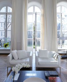 a living room filled with white furniture and large windows