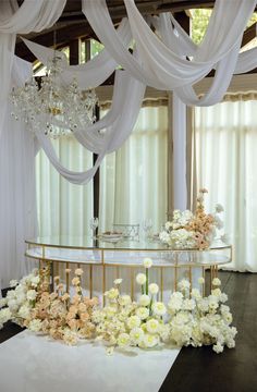 a table with flowers and candles on it in front of white draping curtains