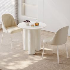 two chairs and a table in a room with white walls, rugs and windows